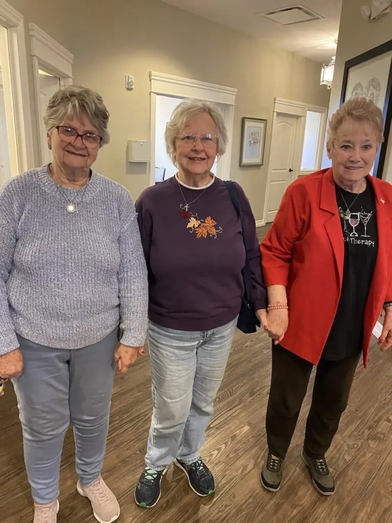 Three senior women smiling together in the hallway of a Colorado senior living community